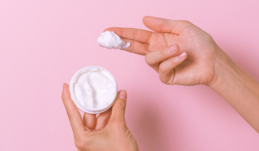 Manos cogiendo una muestra de un bote de crema con dos dedos