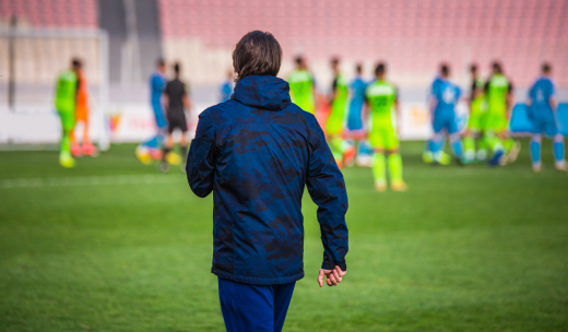 Un entrenador de espalda observando a sus jugadores en el campo de fútbol