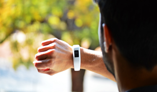Un hombre de espalda mirando el reloj digital que tiene en la mano