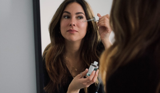 Mujer frente al espejo echándose un producto en la cara