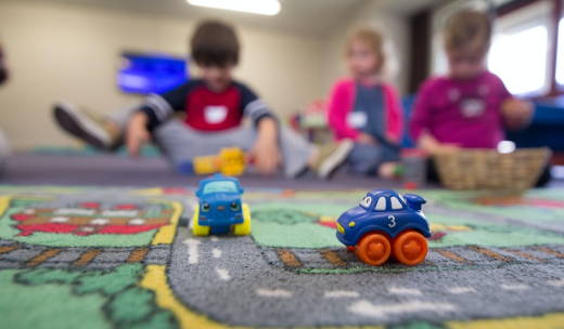 Dos coches de juguete con alfombra y detrás unos niños