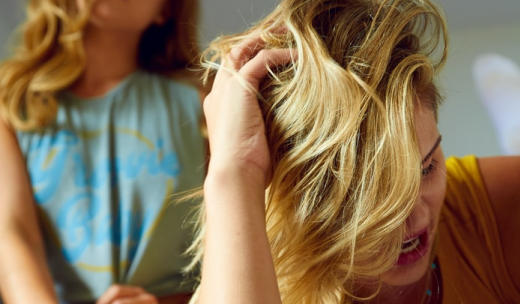 Una mujer rubia tocándose el pelo y otra mujer detrás de ella
