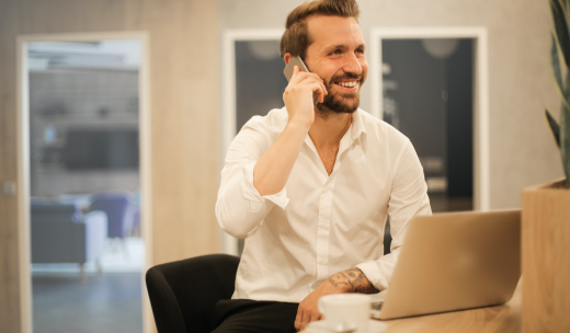 Un hombre en una oficina hablando por teléfono y apoyado en una mesa