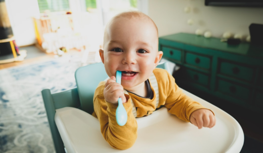 Un bebé sentado en una trona con una cuchara en la boca