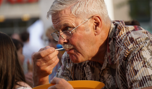 Una persona mayor cogiendo un plato y comiendo algo con una cuchara