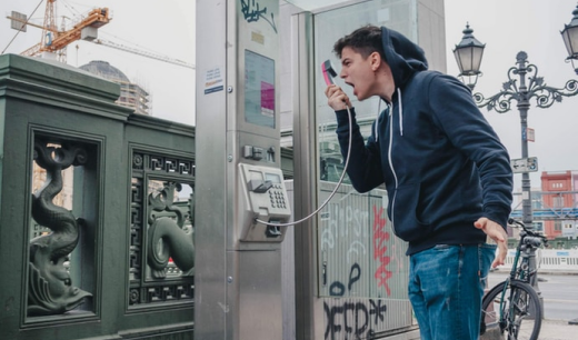 Chico gritando por el auricular de una cabina telefónica