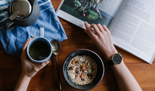 Bol de cereales, taza de café y mano con reloj ojeando un libro