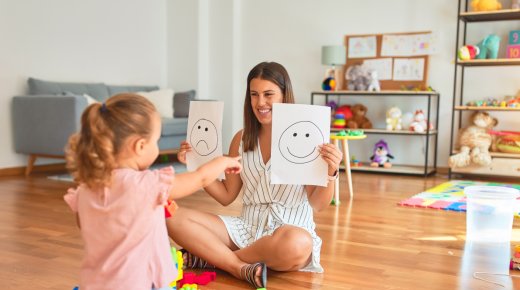 Educadora enseñando dos carteles con caras a una niña para identificar emociones
