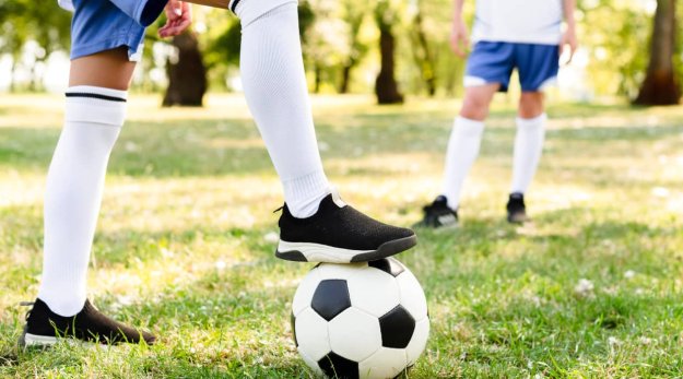 Primer plano de unas piernas de niños jugando al fútbol en un césped