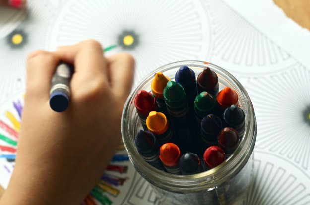 bote de ceras de colores junto a la mano de un niño coloreando