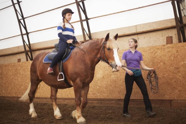 una guía ecuestre enseñando a montar a caballo a una niña