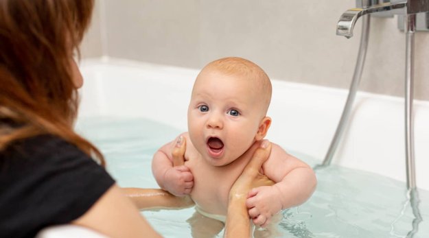 Primer plano de un bebé en una bañera cogido por los brazos