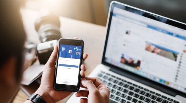 Una persona sujetando el móvil con sus manos y en la pantalla se ve la app de Facebook