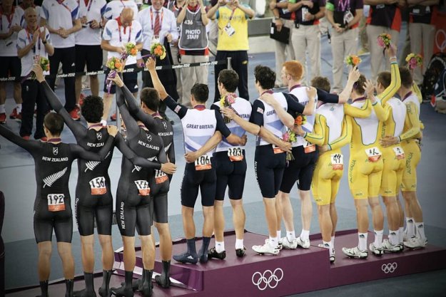 Atletas de Reino Unido, Australia y Nueva Zelanda de espaldas saludando al público en un podio olímpico