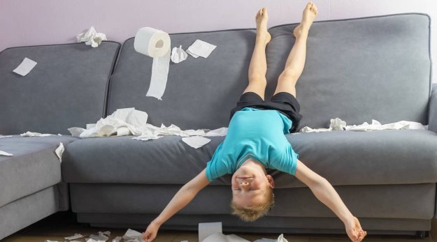 Niño tumbado bocabajo en un sofá y alrededor tiene rollos de papel higiénico 
