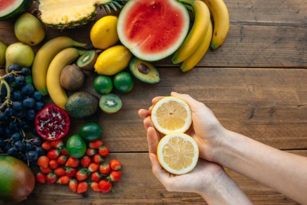 mesa con frutas que contienen vitamina C y una mano sosteniendo las dos mitades de una naranja